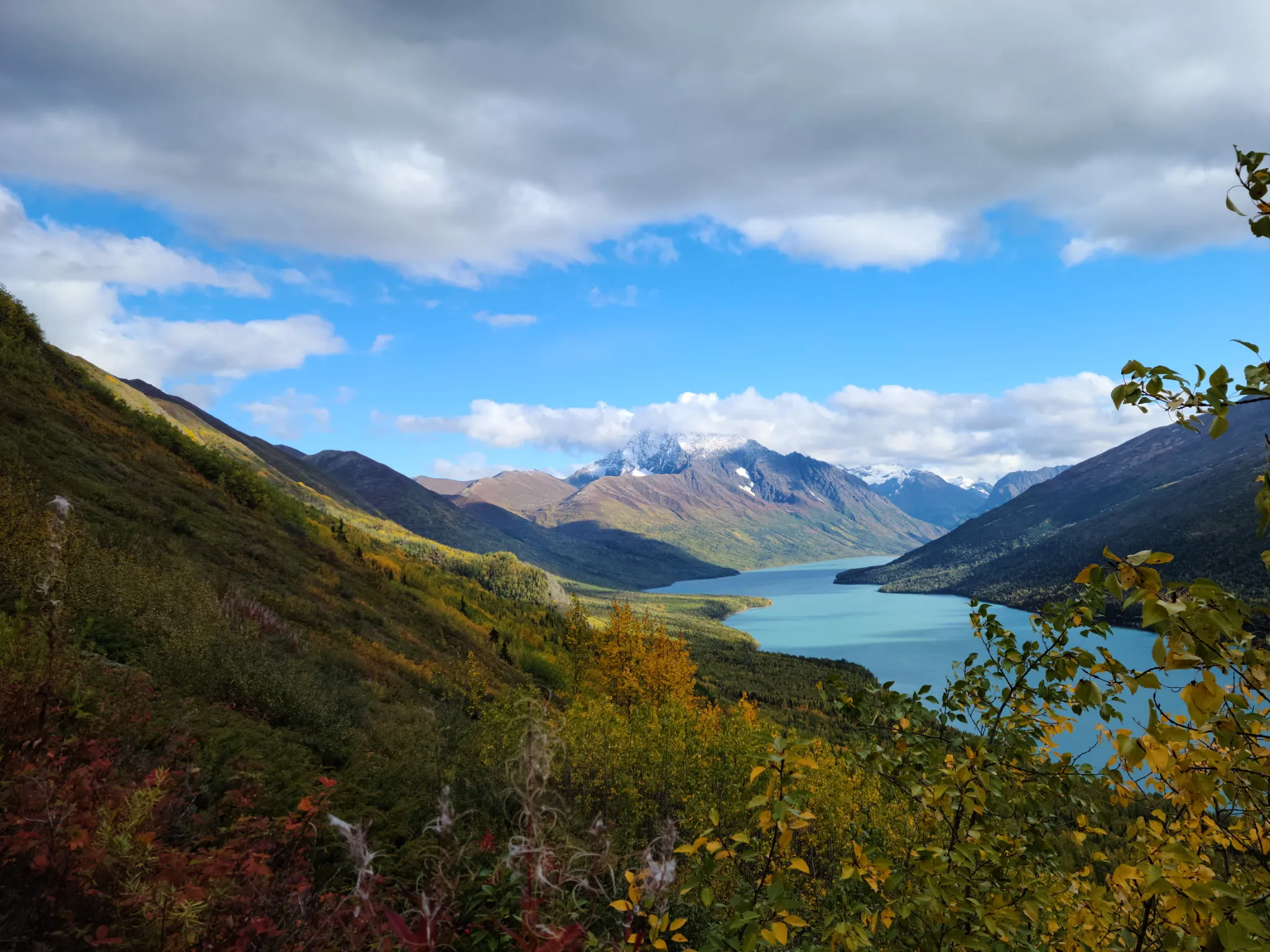 A turquoise glacial lake below snow-dusted peaks in the Chugach, fall color on the slopes